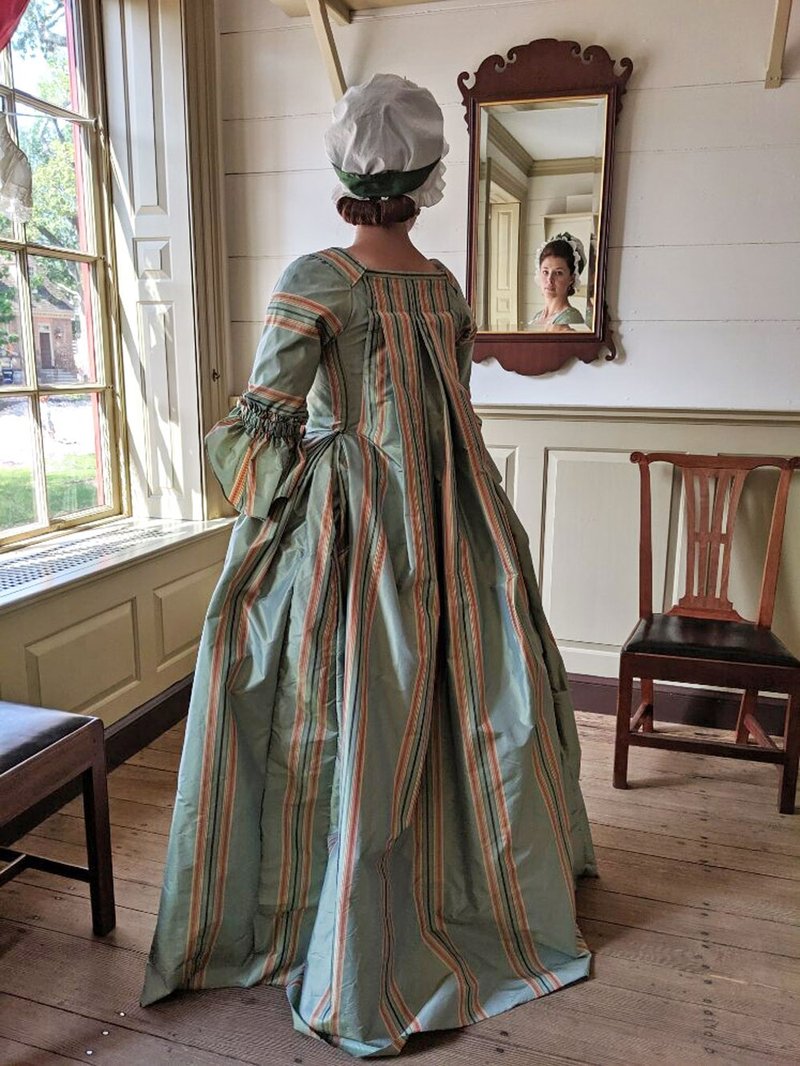 A photo of a woman in an 18th century green and orange dress.