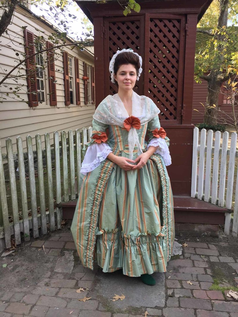 A photo of a woman in an 18th century green and orange dress.