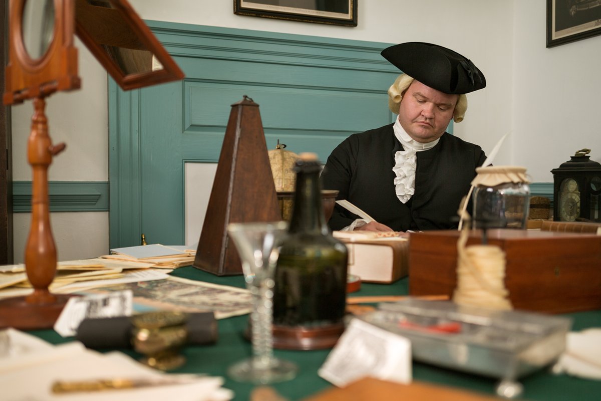 An interpreter dressed as George Wythe works at his desk.