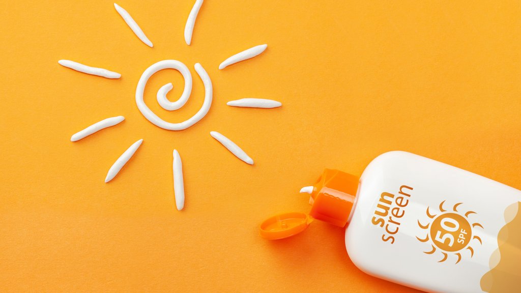 Sunscreen on orange background. Plastic bottle of sun protection and white sun-shaped cream.