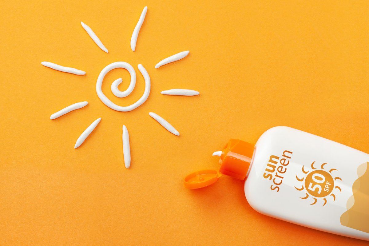 Sunscreen on orange background. Plastic bottle of sun protection and white sun-shaped cream.