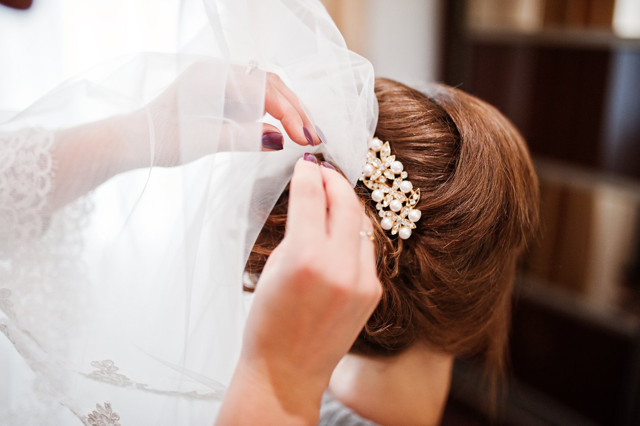 Bridesmaid pinning veil to bride's hair before the wedding.