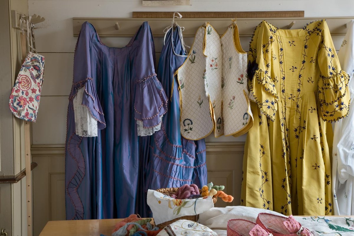 A photo of colorful dresses and other clothing garments hanging on wall hooks.