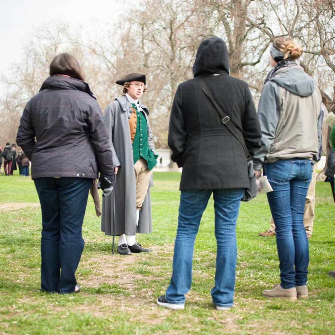 An interpreter dressed as George Mason speaks to a tour group on the Palace Green.